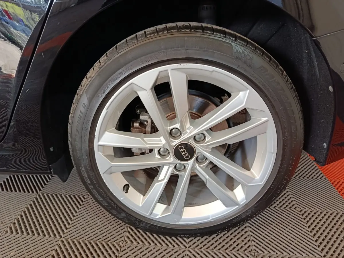 Gros plan sur la roue avant droite d'une Audi A3 noire, jante alliage argentée à 5 doubles branches.