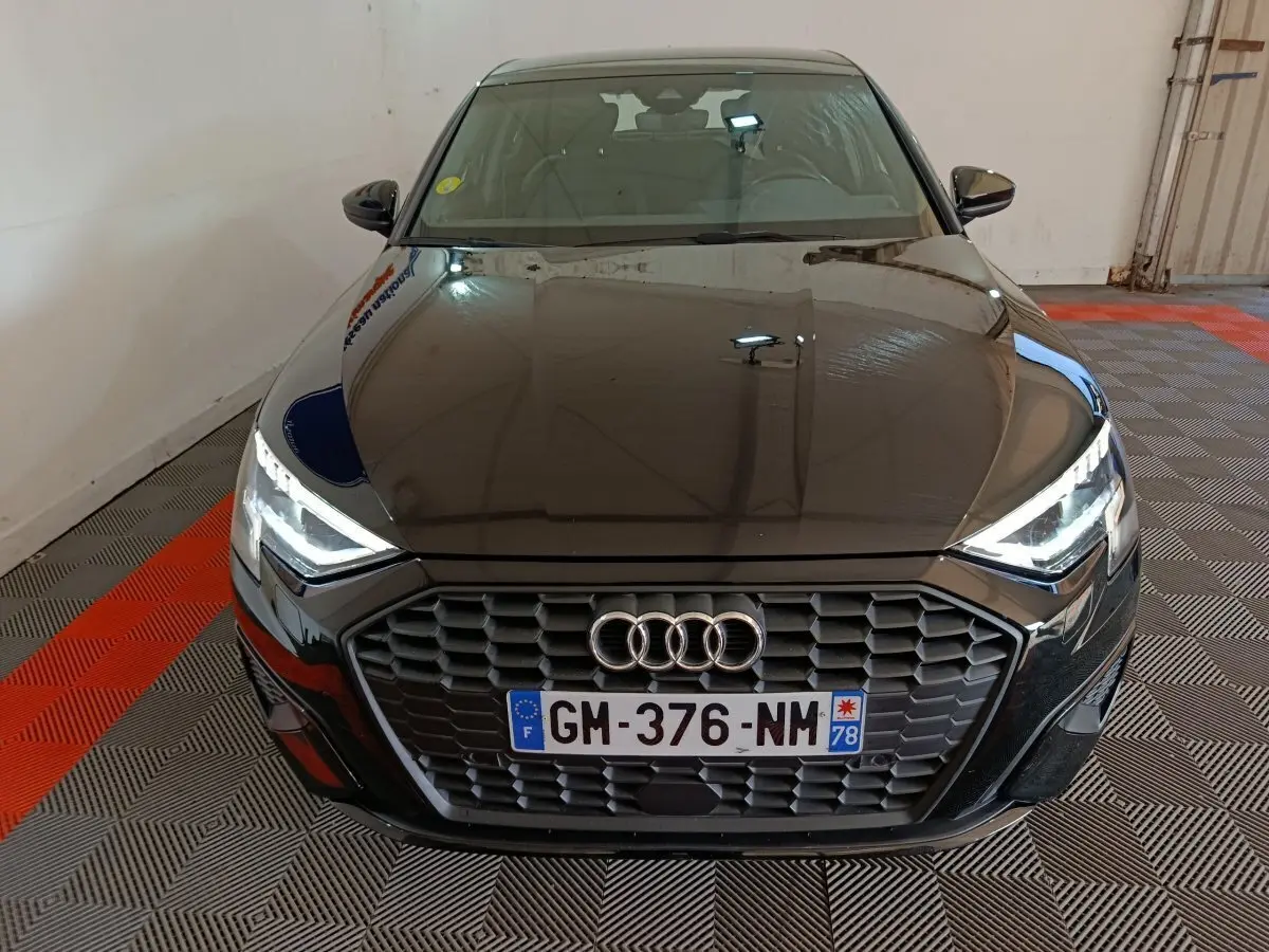 Vue avant d’une Audi A3 35 TDI noire avec calandre hexagonale et phares LED allumés dans un garage.