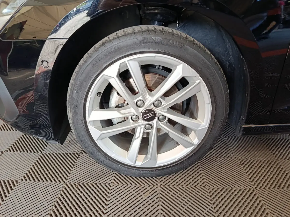 Gros plan sur la roue avant gauche avec jante argentée et logo Audi sur une Audi A3 noire 2023.