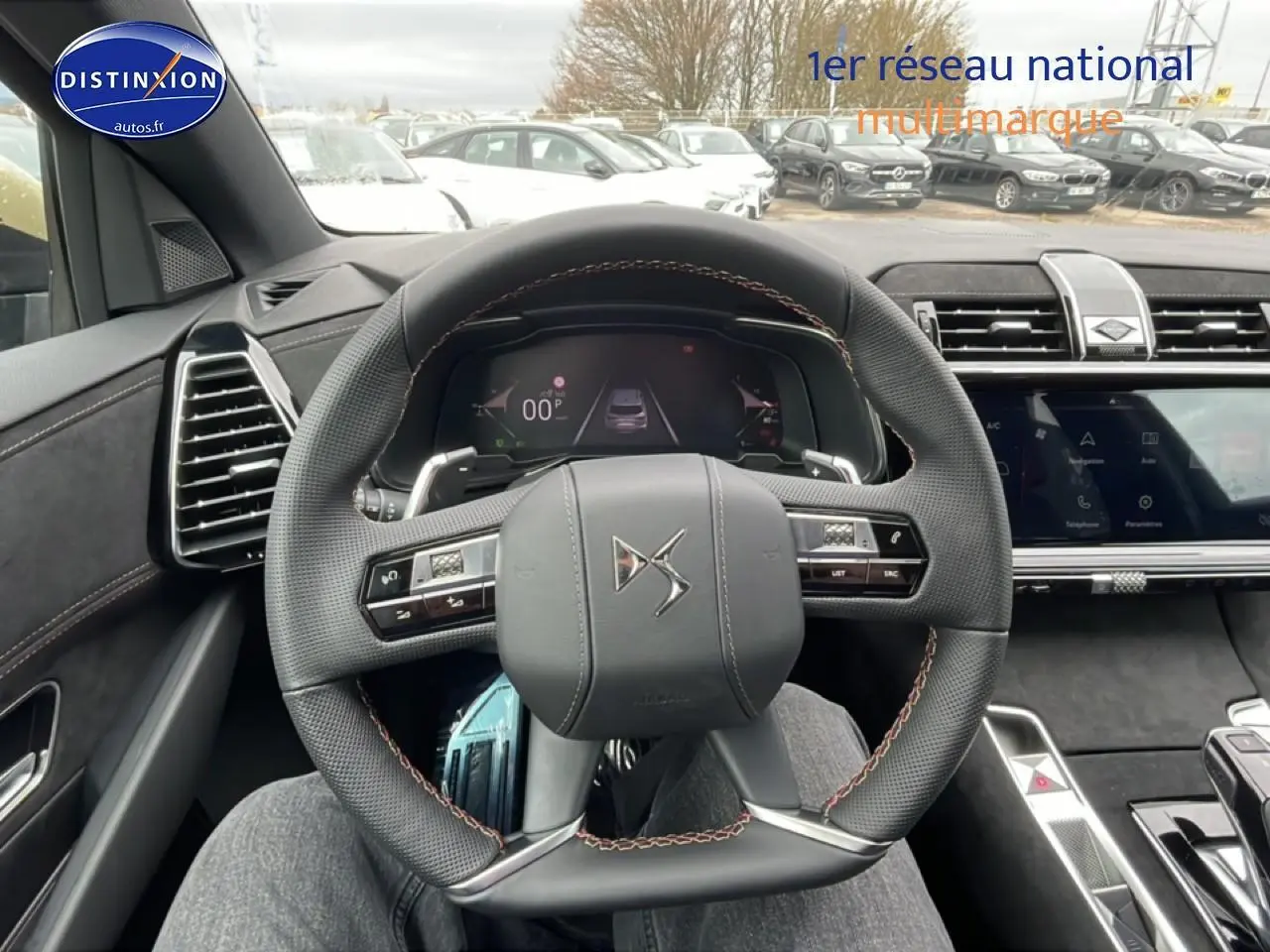 Vue intérieure centrée sur le volant cuir DS d'un DS7 gris titane, avec tableau de bord numérique et écran tactile.