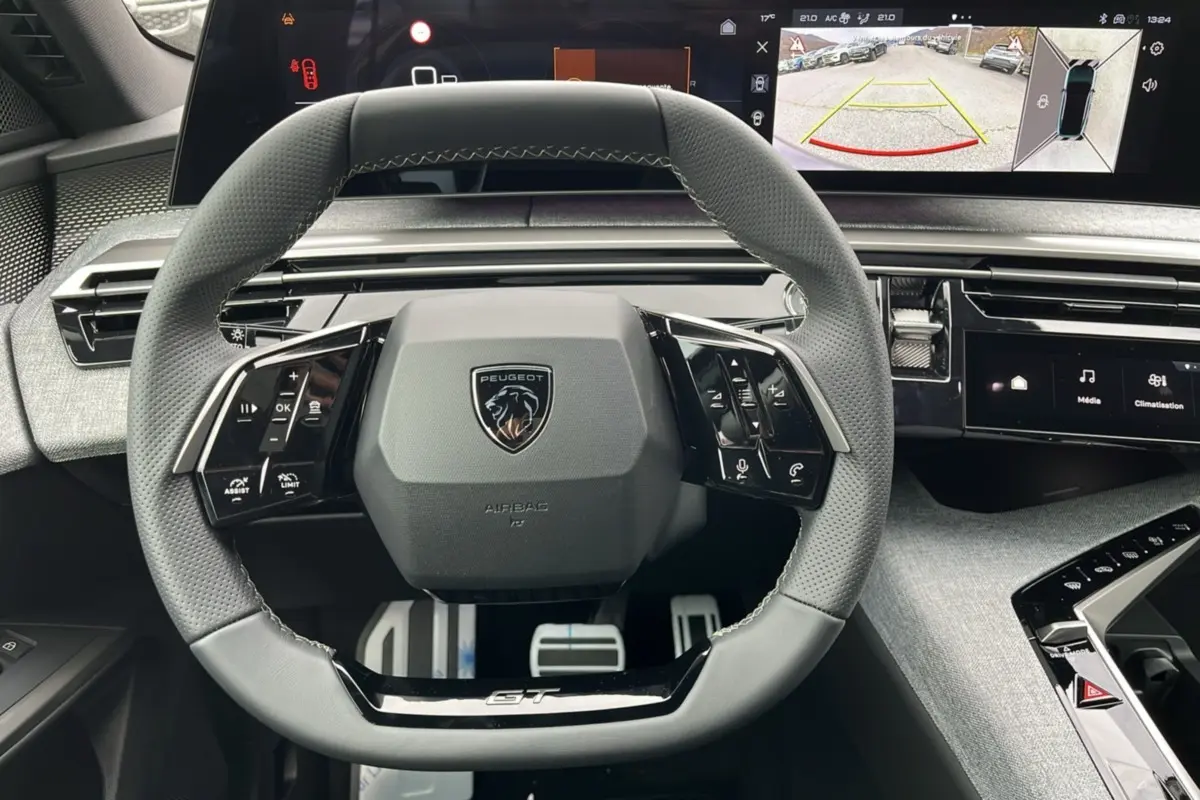 Volant cuir perforé gris avec logo Peugeot et inscription GT, tableau de bord digital affichant caméra de recul du Peugeot 3008 Hybrid.
