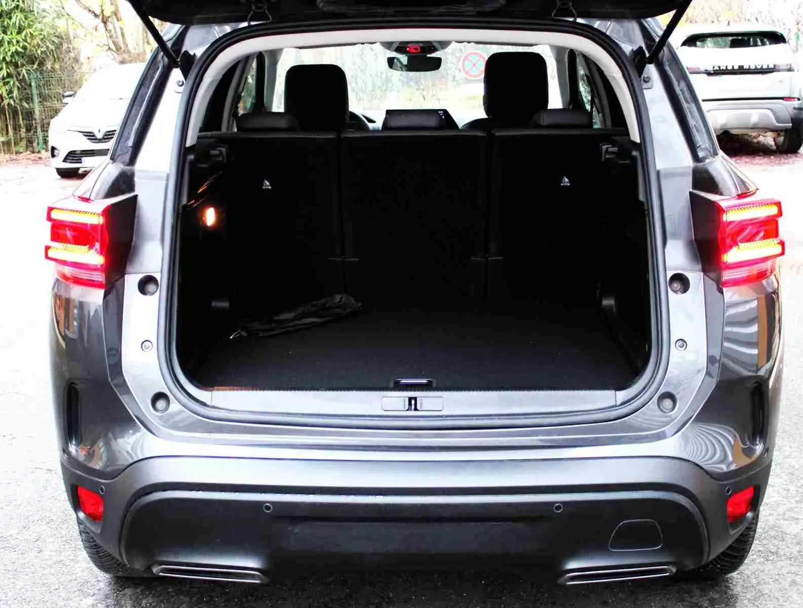 Coffre ouvert d’un Citroën C5 Aircross gris platinium vu de l’arrière, feux arrière allumés et intérieur spacieux.