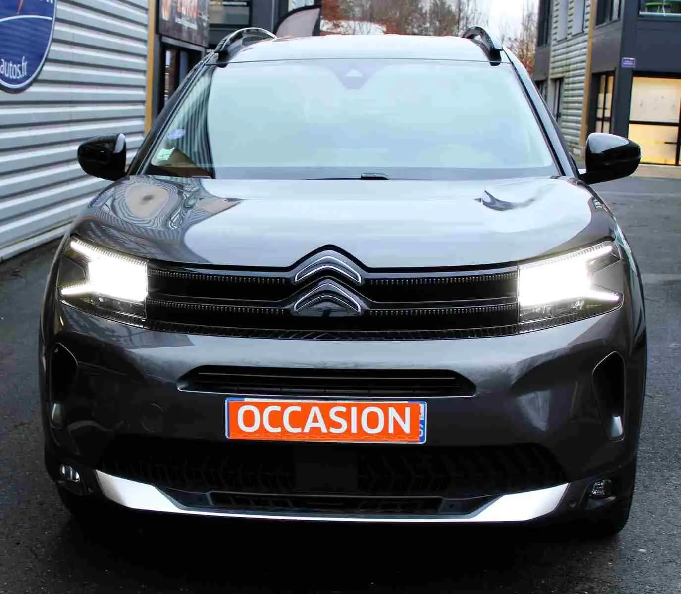 Vue frontale d'un Citroën C5 Aircross gris platinium avec phares allumés et plaque "OCCASION" orange visible.
