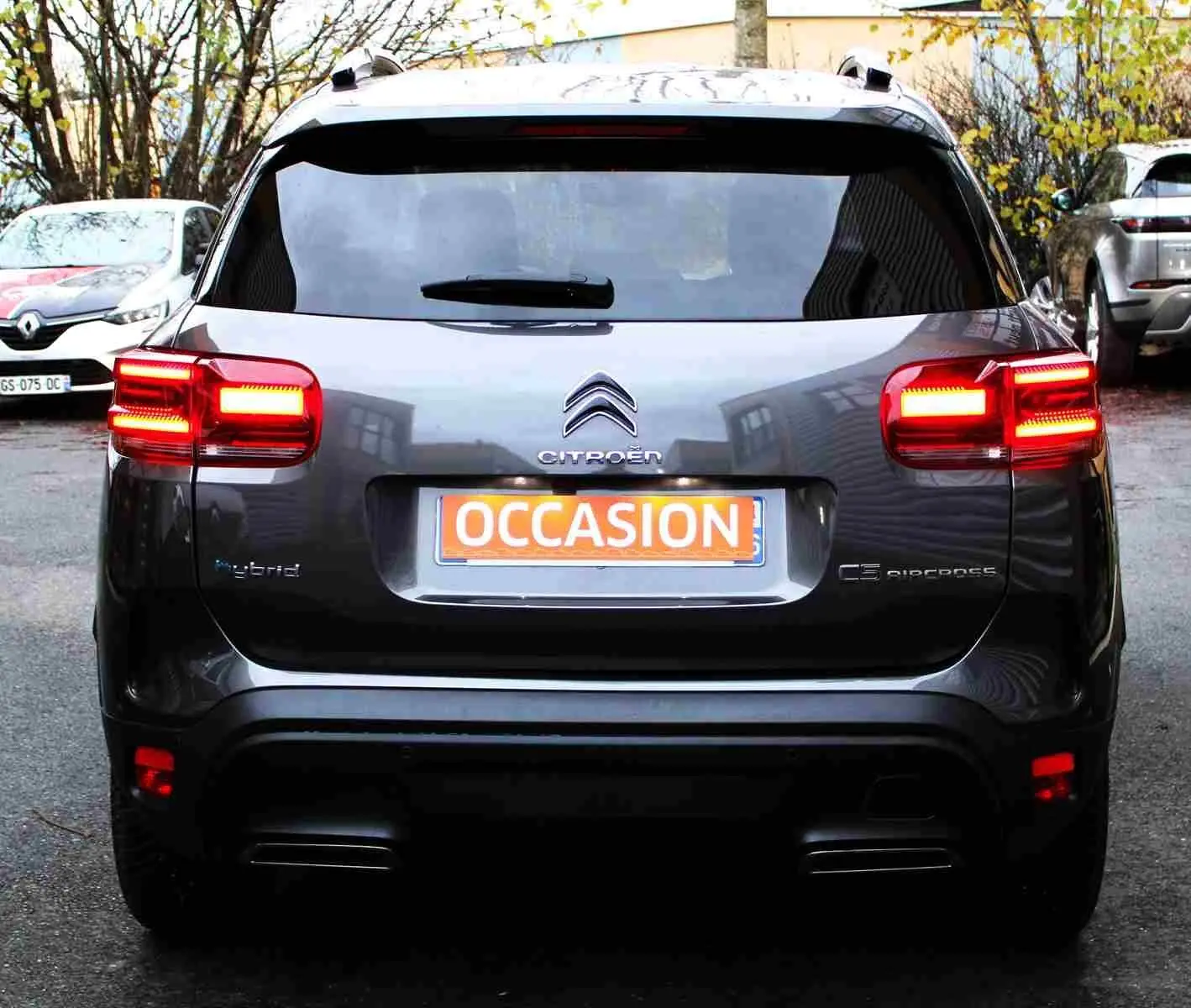 Vue arrière d'un Citroën C5 Aircross gris platinium hybride rechargeable avec feux arrière allumés et plaque "OCCASION".