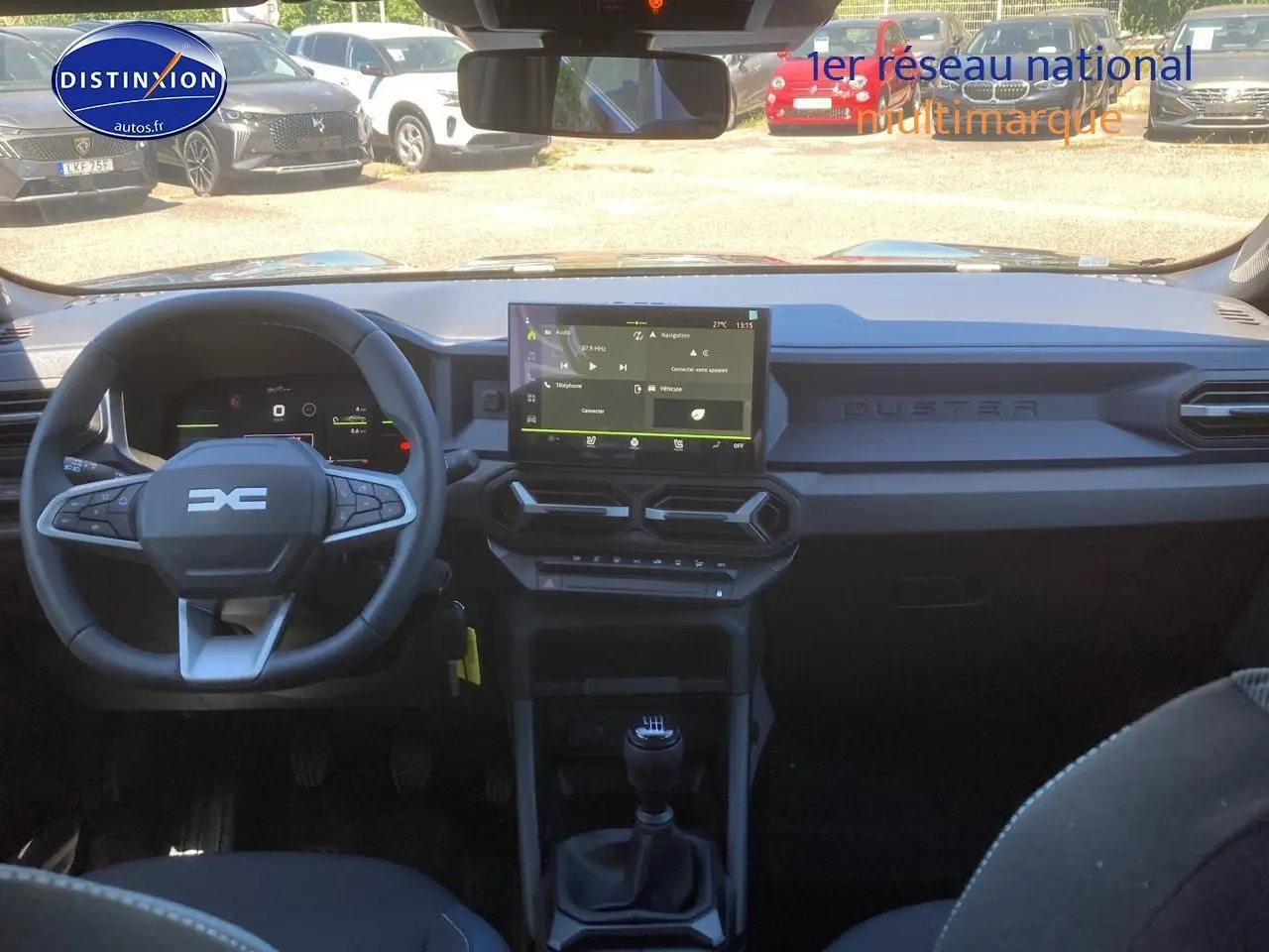 Vue intérieure frontale du tableau de bord noir du Dacia Duster 2025 avec écran tactile et volant multifonction.