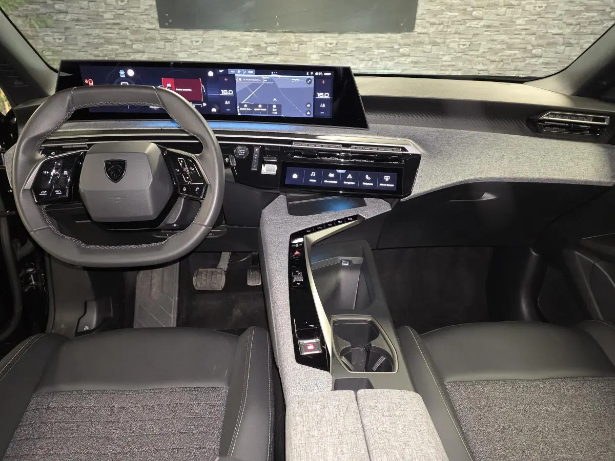 Vue intérieure avant du Peugeot 5008 2025 hybride, tableau de bord moderne avec double écran HD et volant compact cuir noir.