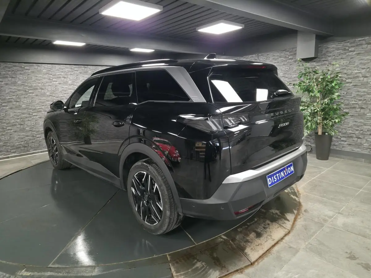 Vue 3/4 arrière droit d’un Peugeot 5008 noir brillant avec jantes alliage noires et vitres teintées en intérieur showroom.