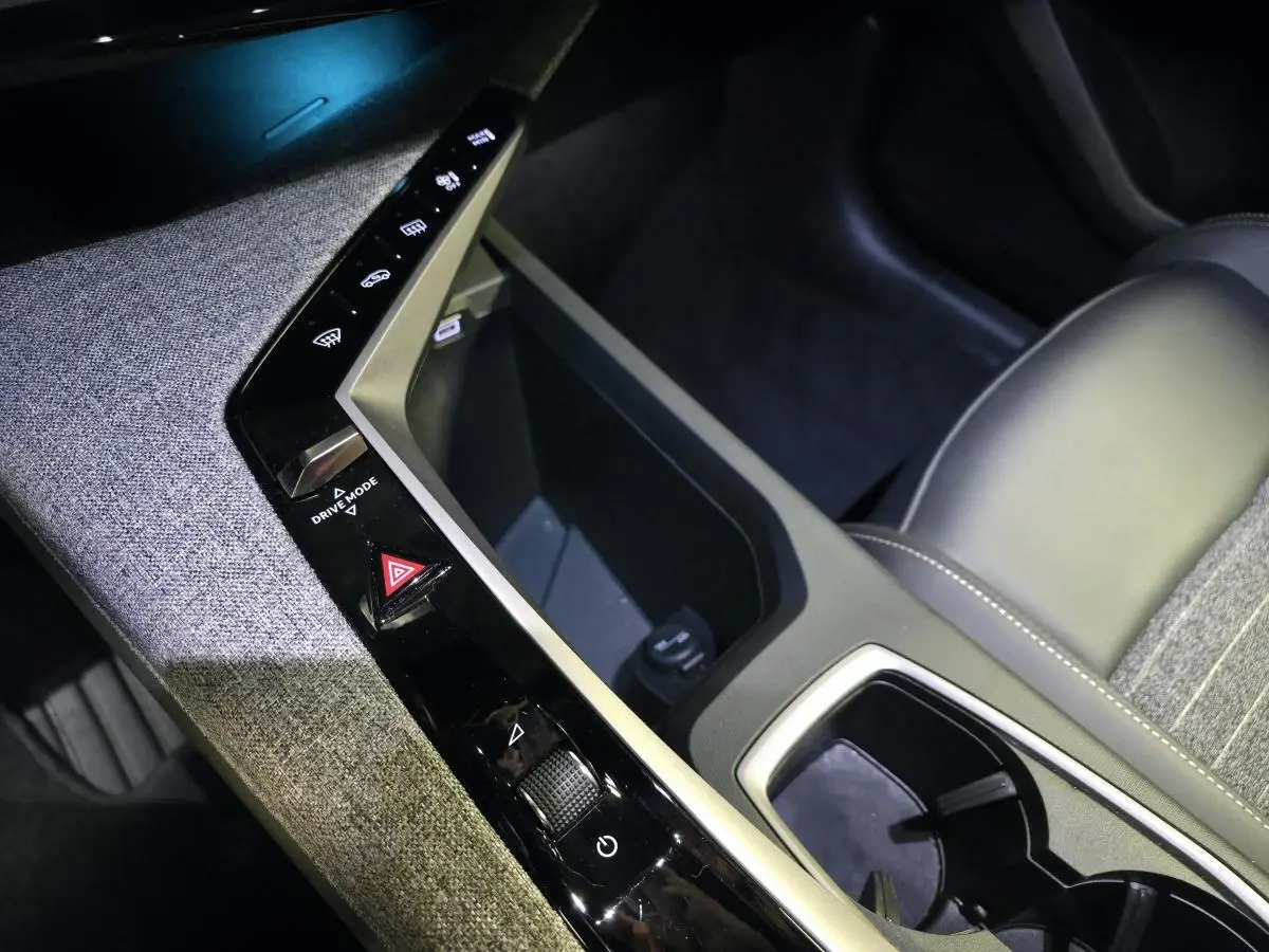 Détail de la console centrale avec commandes tactiles et rangement, sellerie tissu gris et cuir noir du Peugeot 5008 hybride 2025.