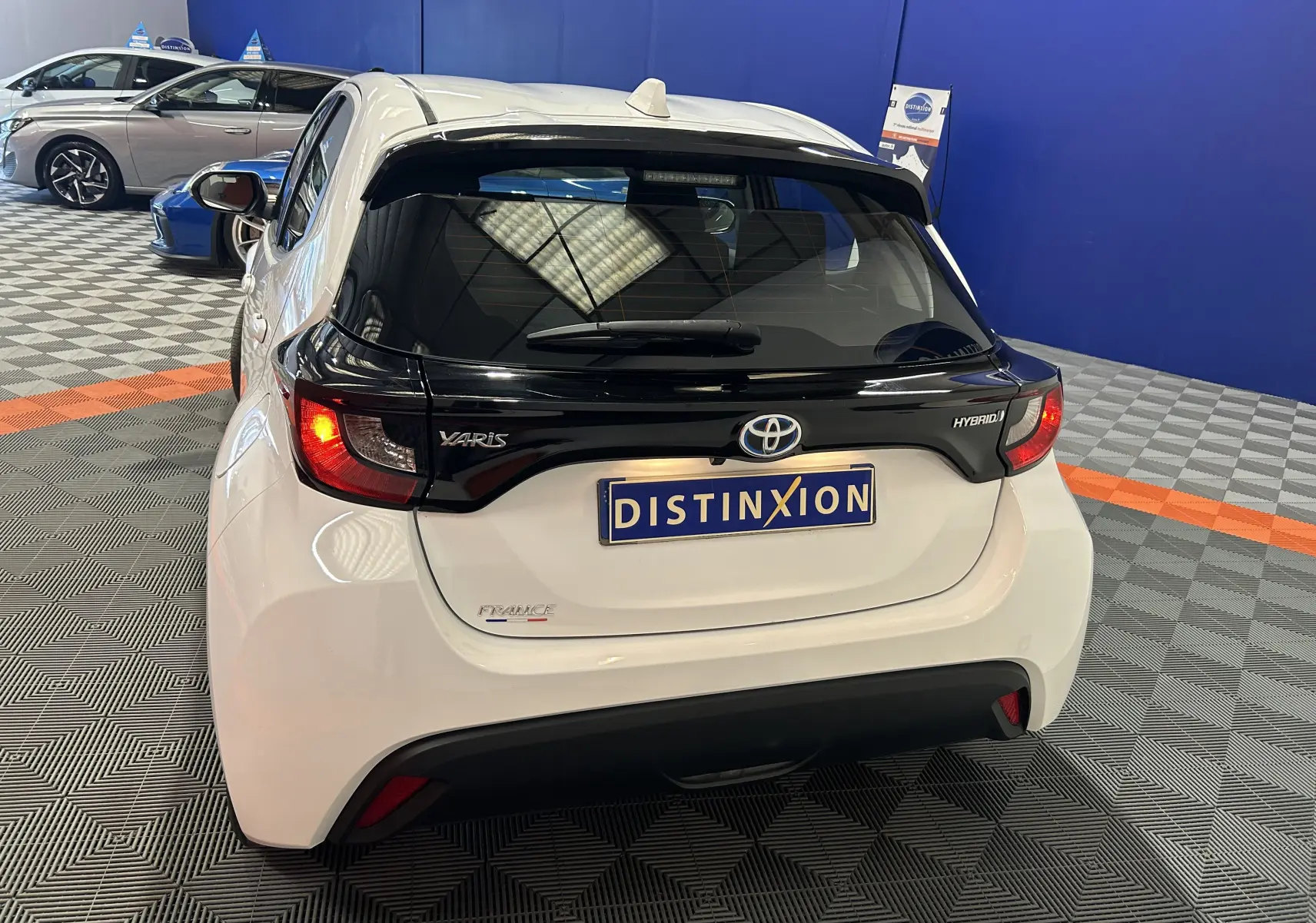 Vue arrière d'une Toyota Yaris hybride blanche avec toit noir et feux arrière allumés dans un showroom.