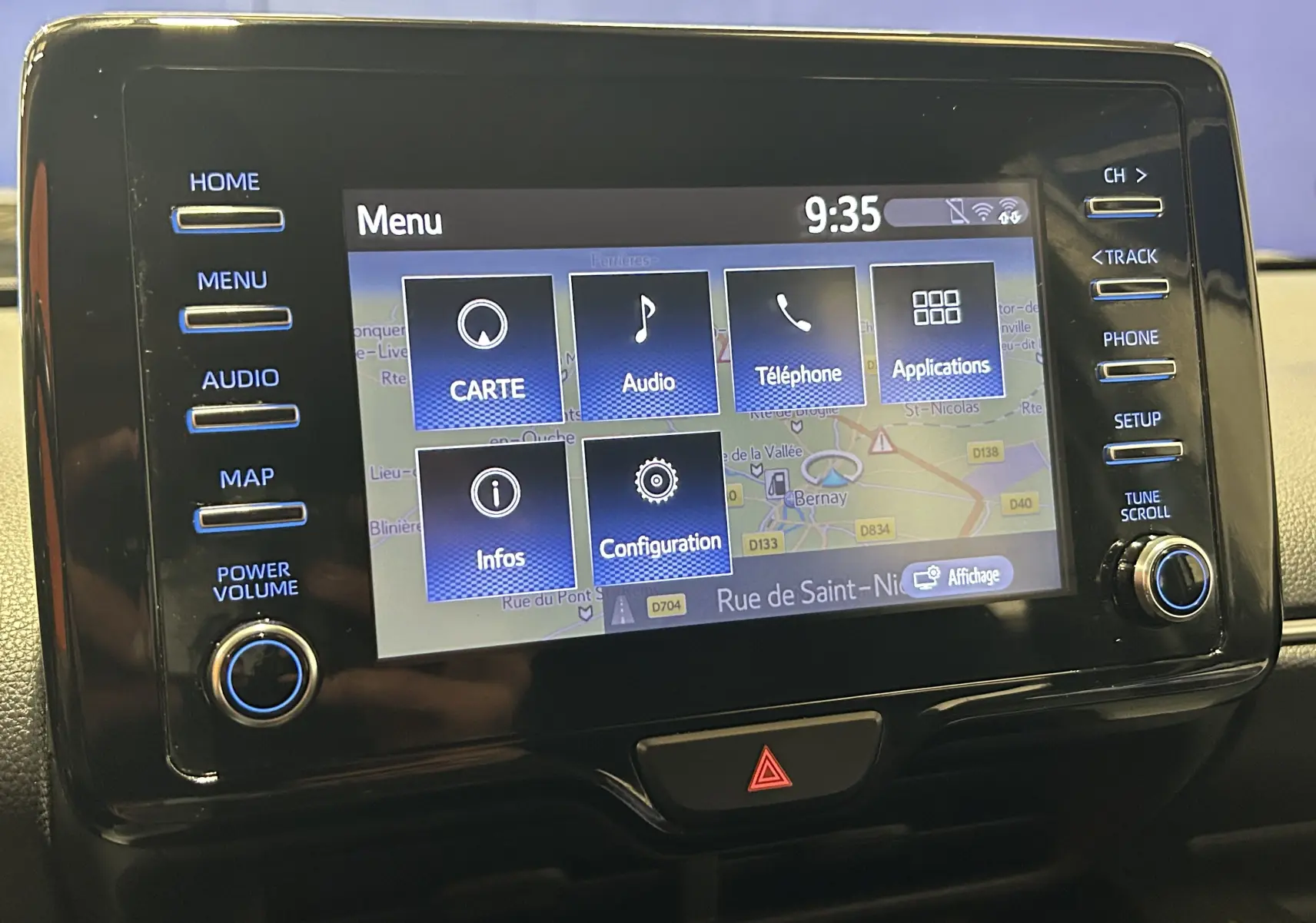 Écran tactile central de la Toyota Yaris 116h blanc, affichant le menu GPS avec boutons latéraux et bouton d’alerte en dessous.