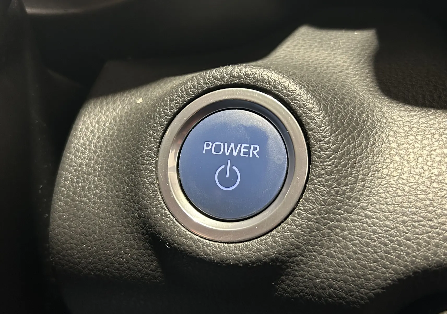 Gros plan sur le bouton start/stop bleu entouré de noir dans l’habitacle de la Toyota Yaris hybride blanche 2021.