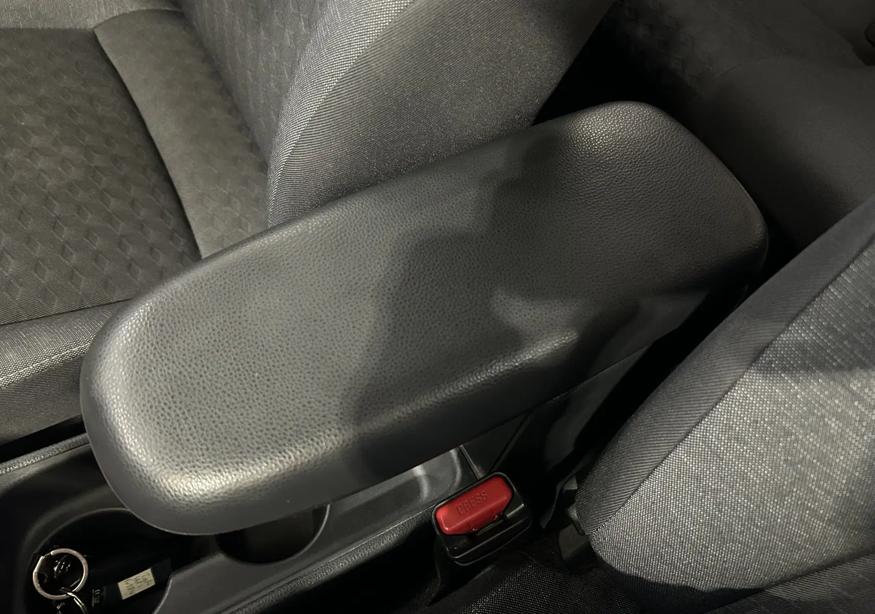 Gros plan sur l'accoudoir central noir et les sièges en tissu gris à l'intérieur de la Toyota Yaris 116h blanche.