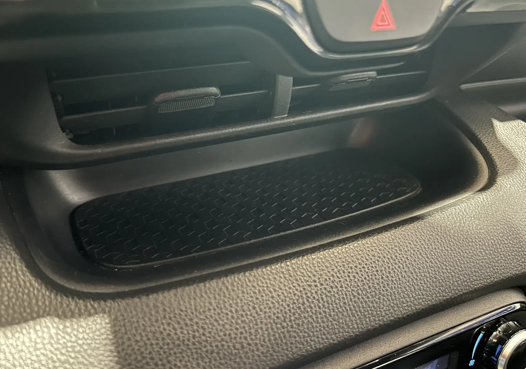 Détail de la console centrale noire de la Toyota Yaris 116h blanche, mettant en valeur un rangement avec surface antidérapante.