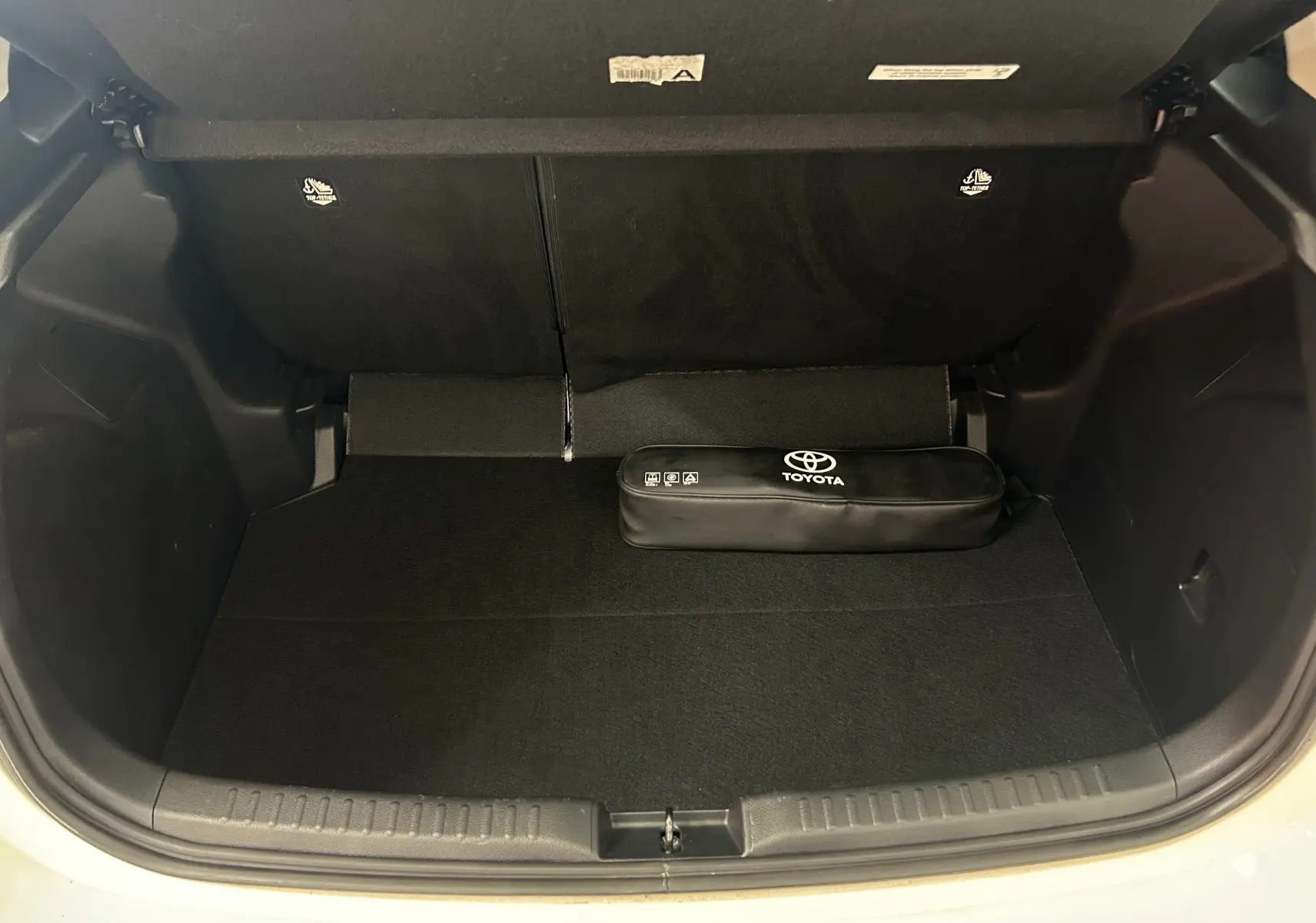 Vue du coffre ouvert d'une Toyota Yaris blanche 2021, avec un kit de secours Toyota noir posé à l'intérieur.