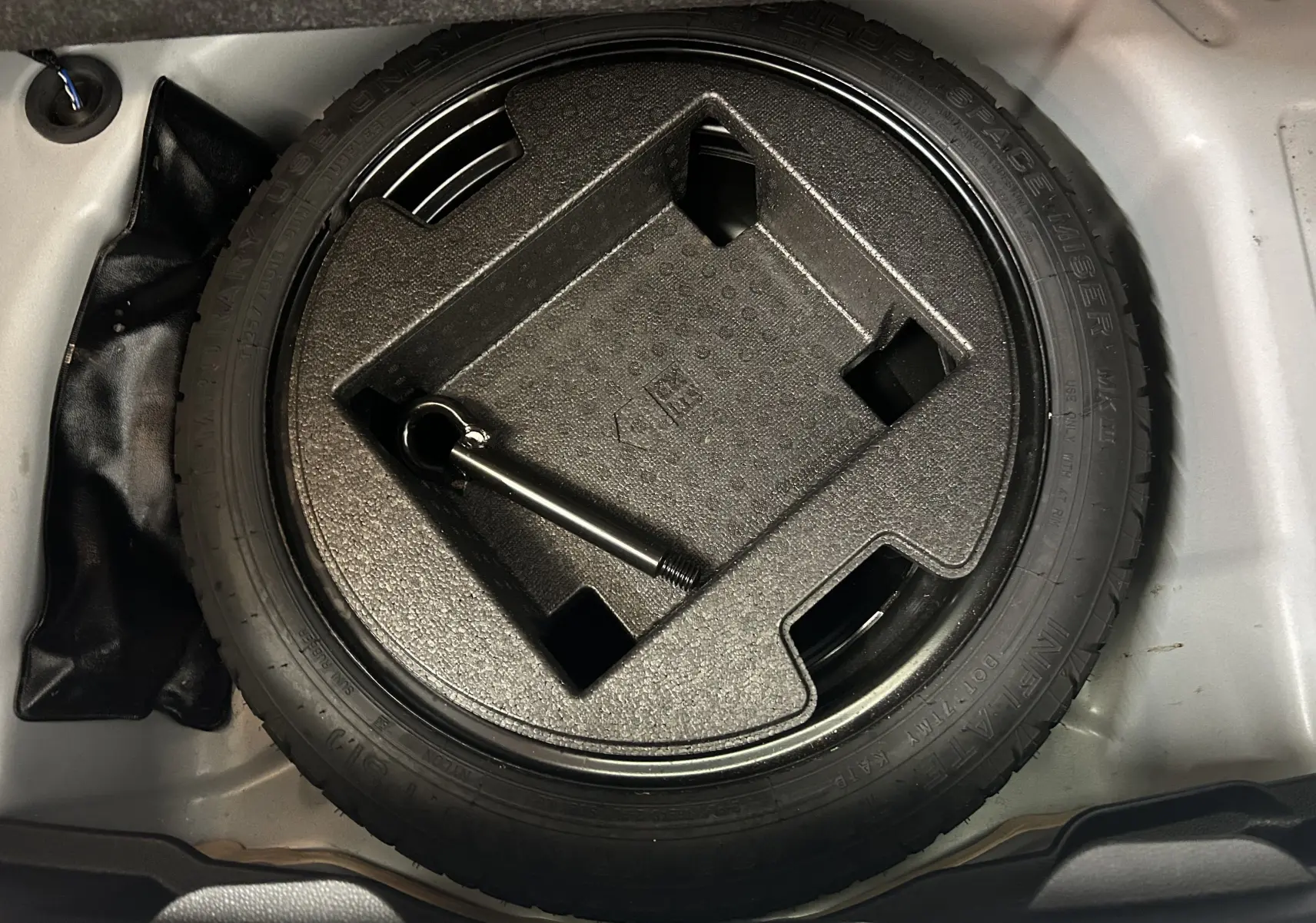 Vue plongeante sur la roue de secours noire et son support en mousse dans le coffre d'une Toyota Yaris blanche 2021.