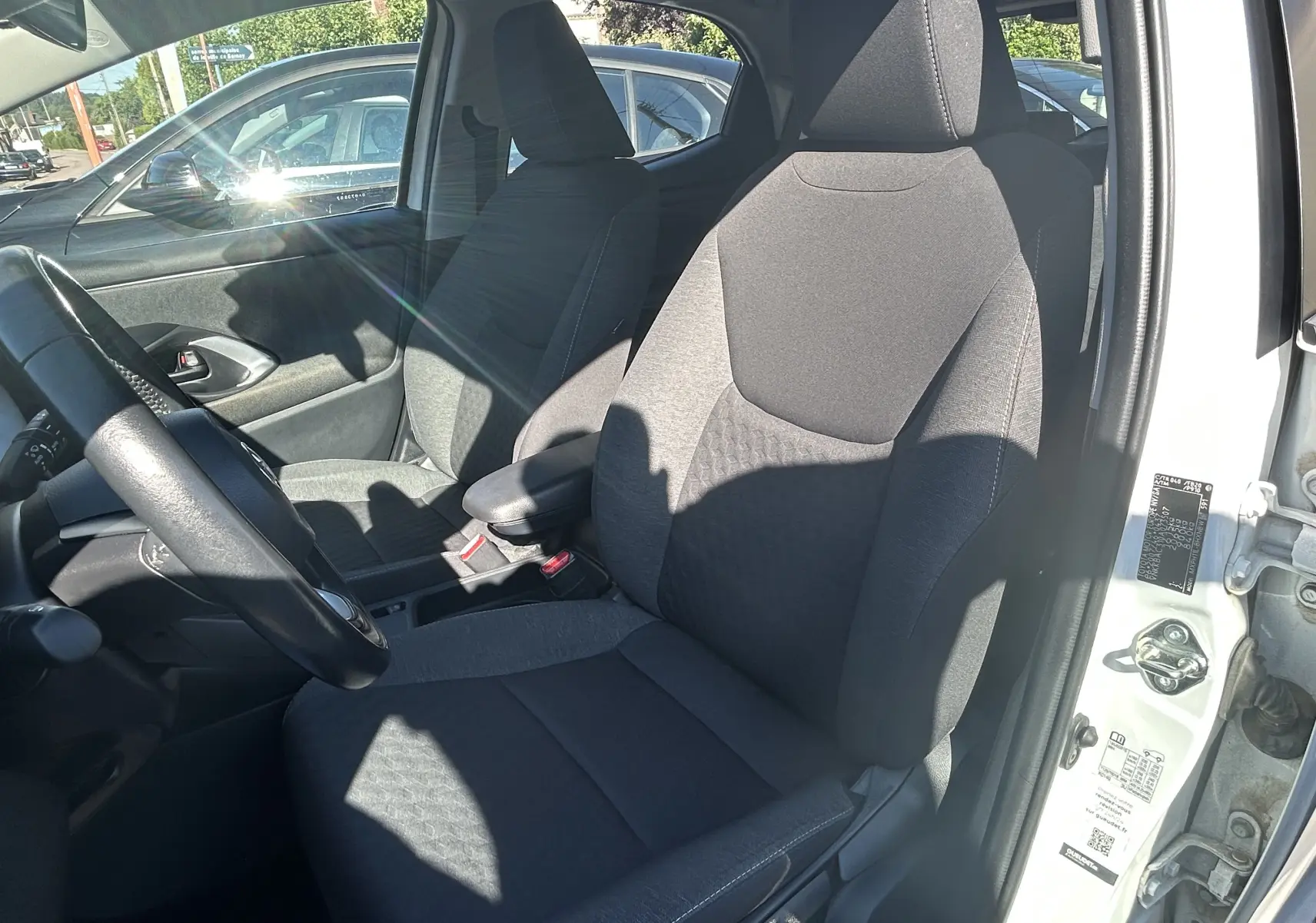 Vue intérieure côté conducteur de la Toyota Yaris blanche 2021, sièges tissu gris et volant multifonction visible.