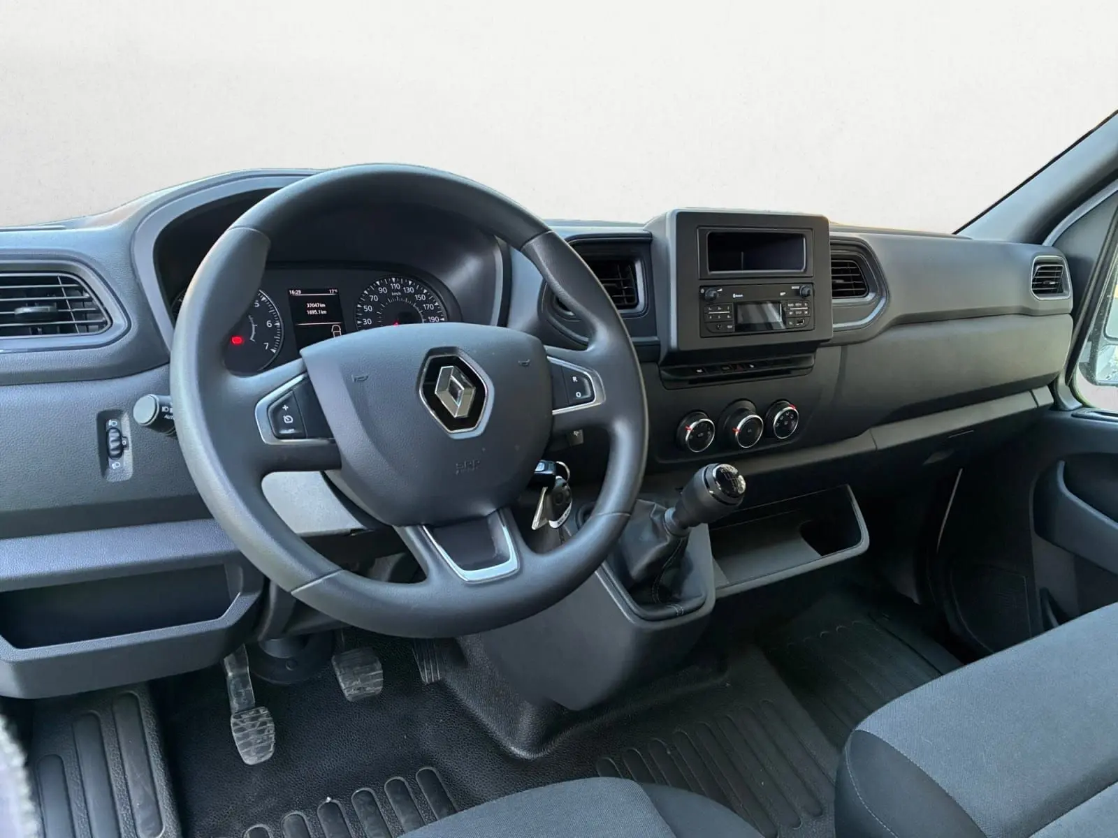Vue intérieure du poste de conduite du Renault Master 2024, volant noir avec logo, tableau de bord et levier de vitesses manuel.