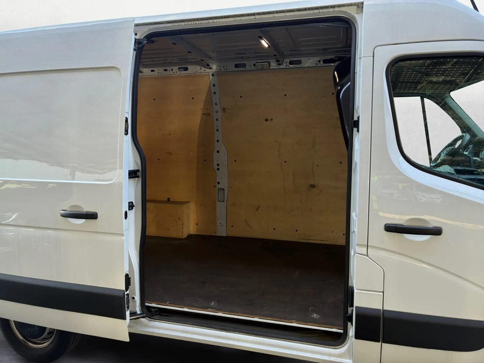 Vue latérale gauche d’un Renault Master blanc 2024 avec porte coulissante ouverte montrant l’intérieur vide en bois.