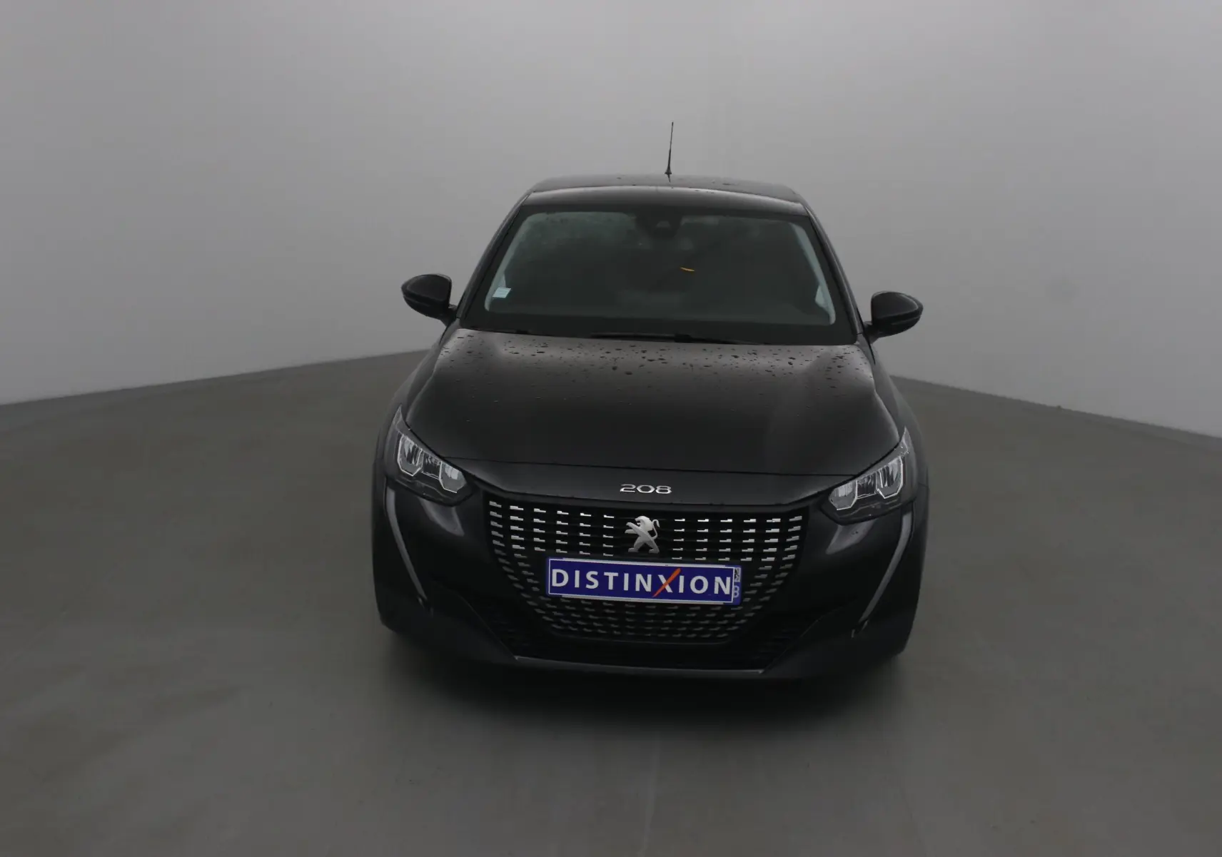 Peugeot 208 noir vue de face, avec calandre distinctive et plaques d'immatriculation "DISTINXION" visibles.