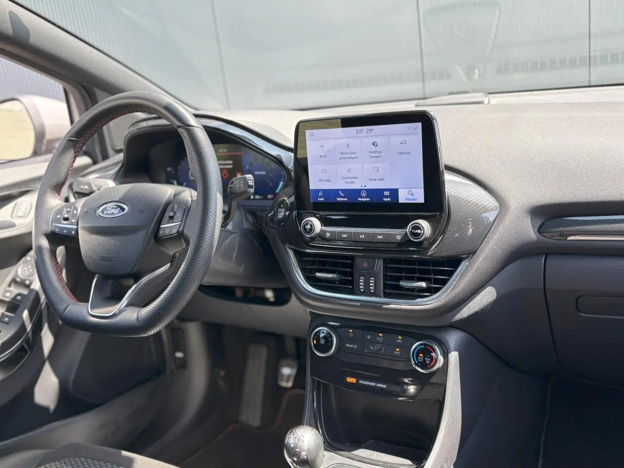 Vue intérieure avant du Ford Puma ST Line 2020, tableau de bord noir avec écran tactile central et volant sport à surpiqûres rouges.