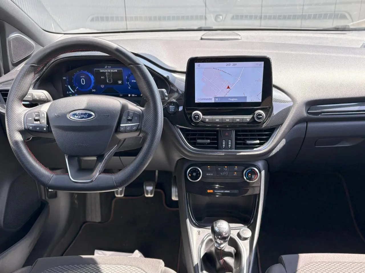 Vue intérieure frontale du tableau de bord du Ford Puma gris Solar, avec écran tactile GPS et volant ST-Line à surpiqûres rouges.