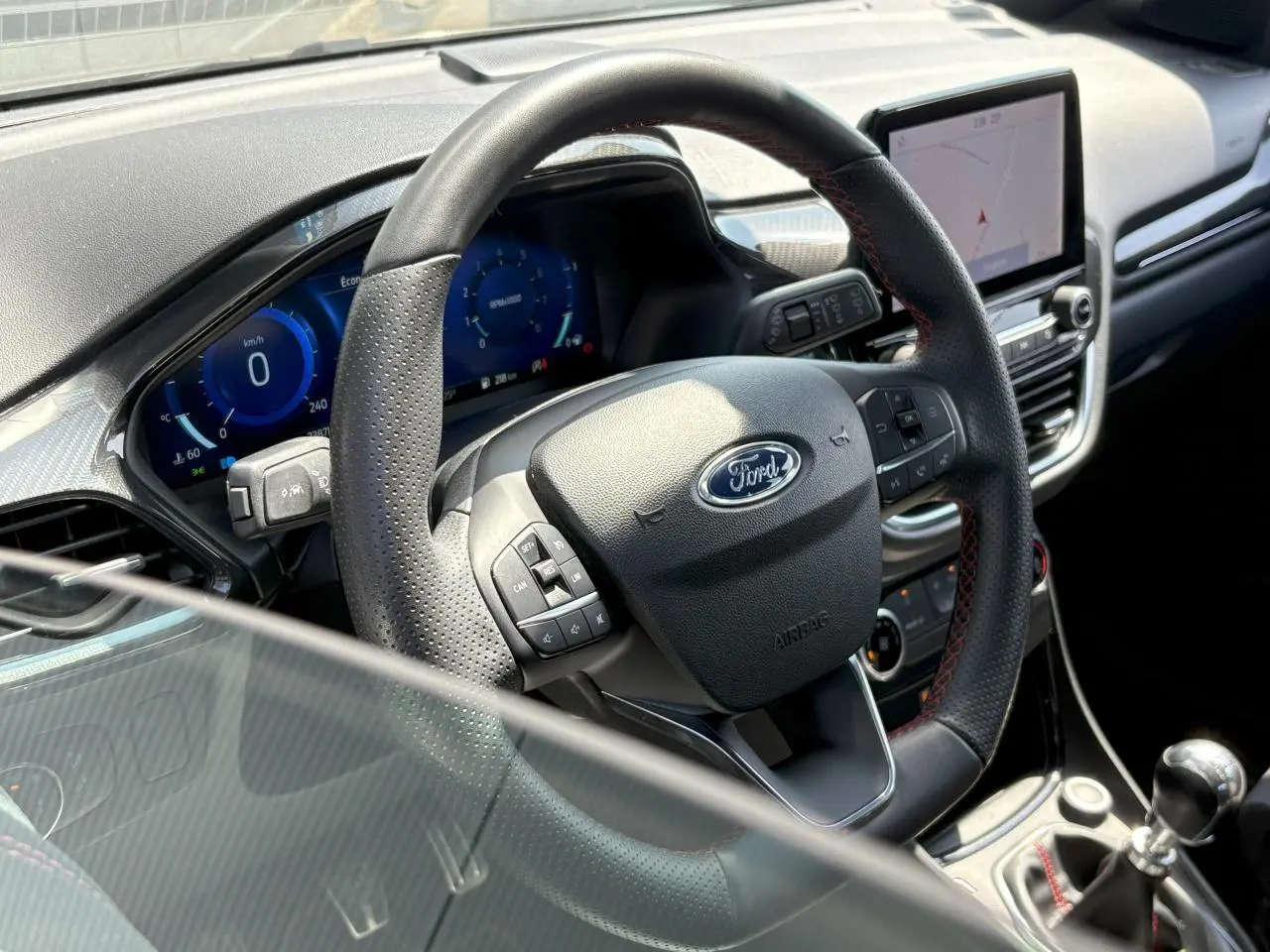 Vue rapprochée du volant noir perforé avec surpiqûres rouges et tableau de bord numérique du Ford Puma Gris Solar 2020.
