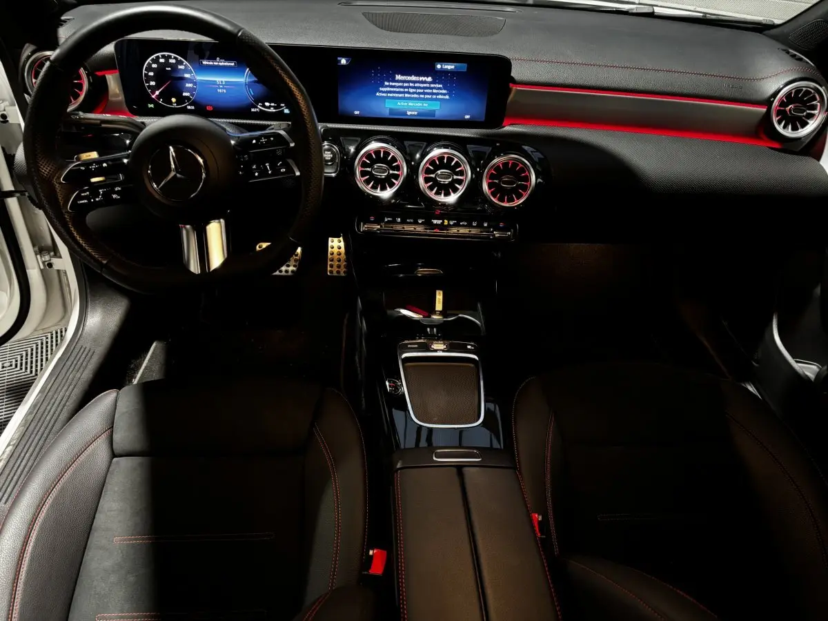 Vue intérieure avant de la Mercedes CLA 250 e AMG Line 2023, tableau de bord noir avec éclairage d’ambiance rouge et écran tactile.