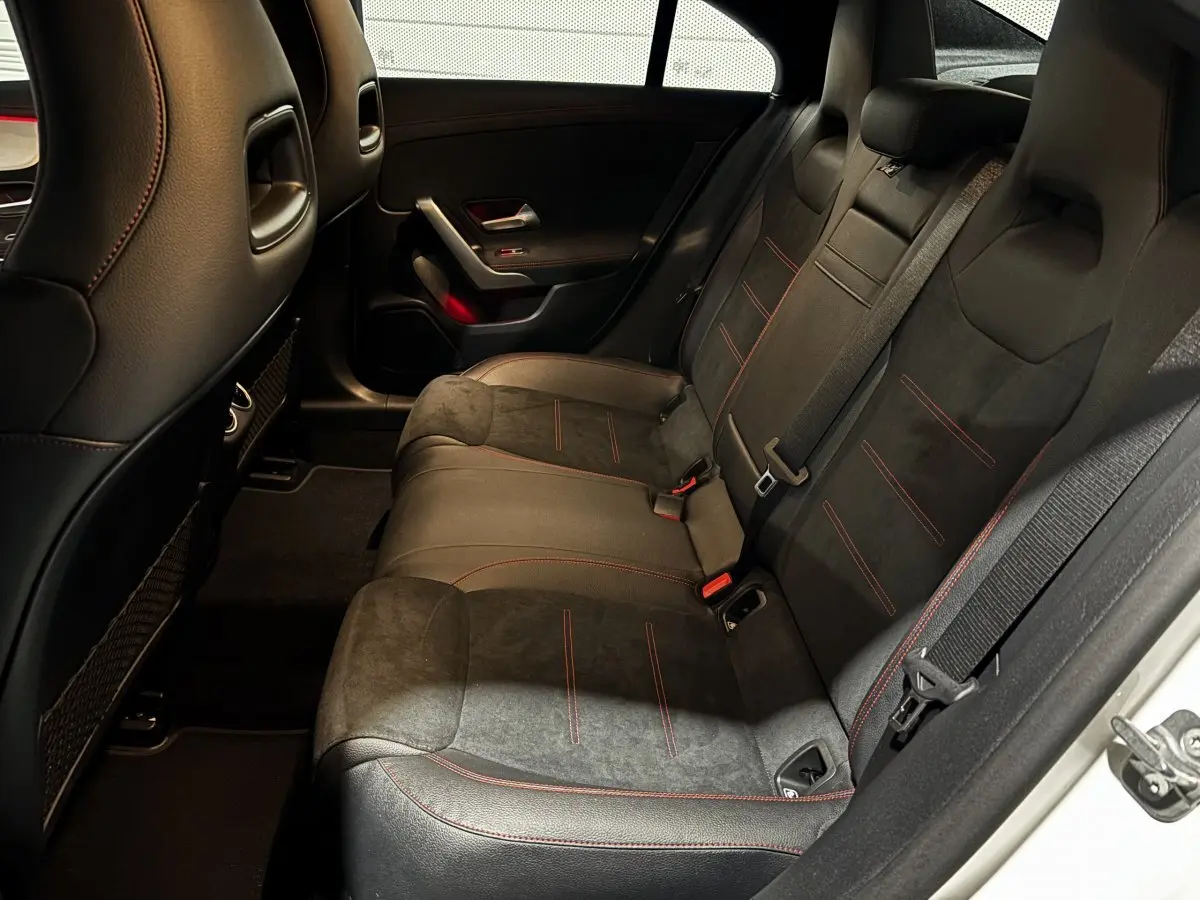 Vue intérieure côté droit des sièges arrière noirs avec surpiqûres rouges dans une Mercedes CLA 250 e AMG Line blanche 2023.