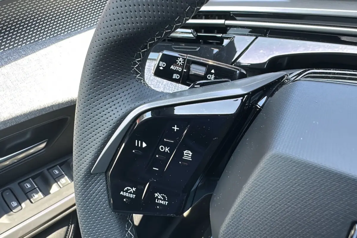 Gros plan sur le volant cuir perforé du Peugeot 3008 Hybrid 145 GT avec commandes multifonctions et bouton assist.