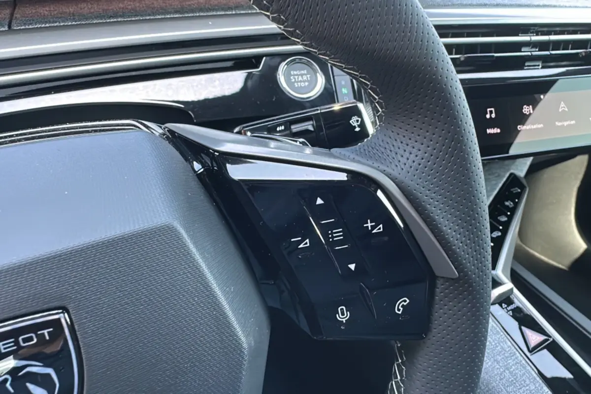 Gros plan sur le volant cuir perforé du Peugeot 3008 Hybrid 145 GT avec commandes multifonctions et bouton start/stop.