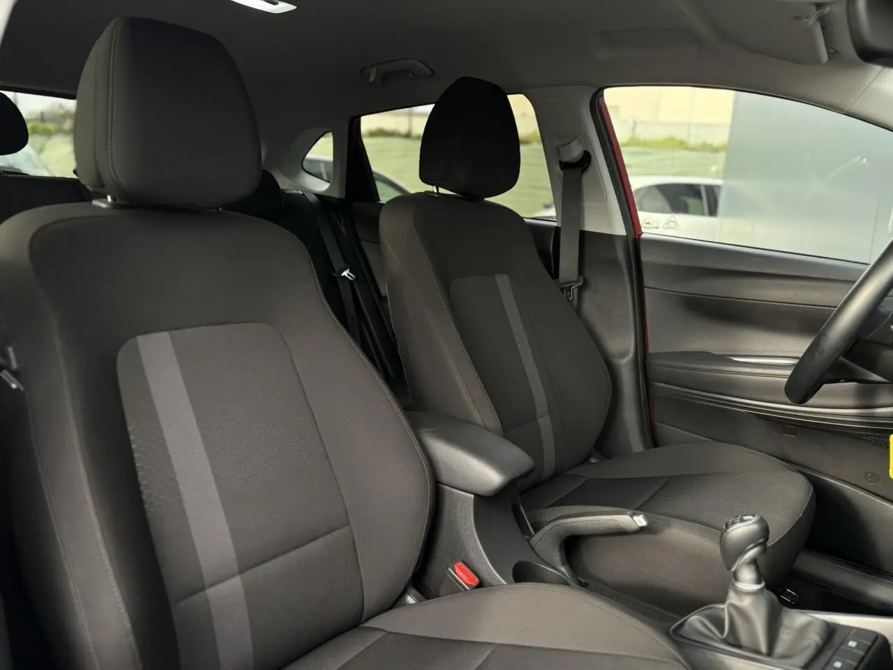 Vue intérieure côté droit montrant les sièges avant noirs et la console centrale d'une Hyundai i20 Rouge Dragon Metal 2025.