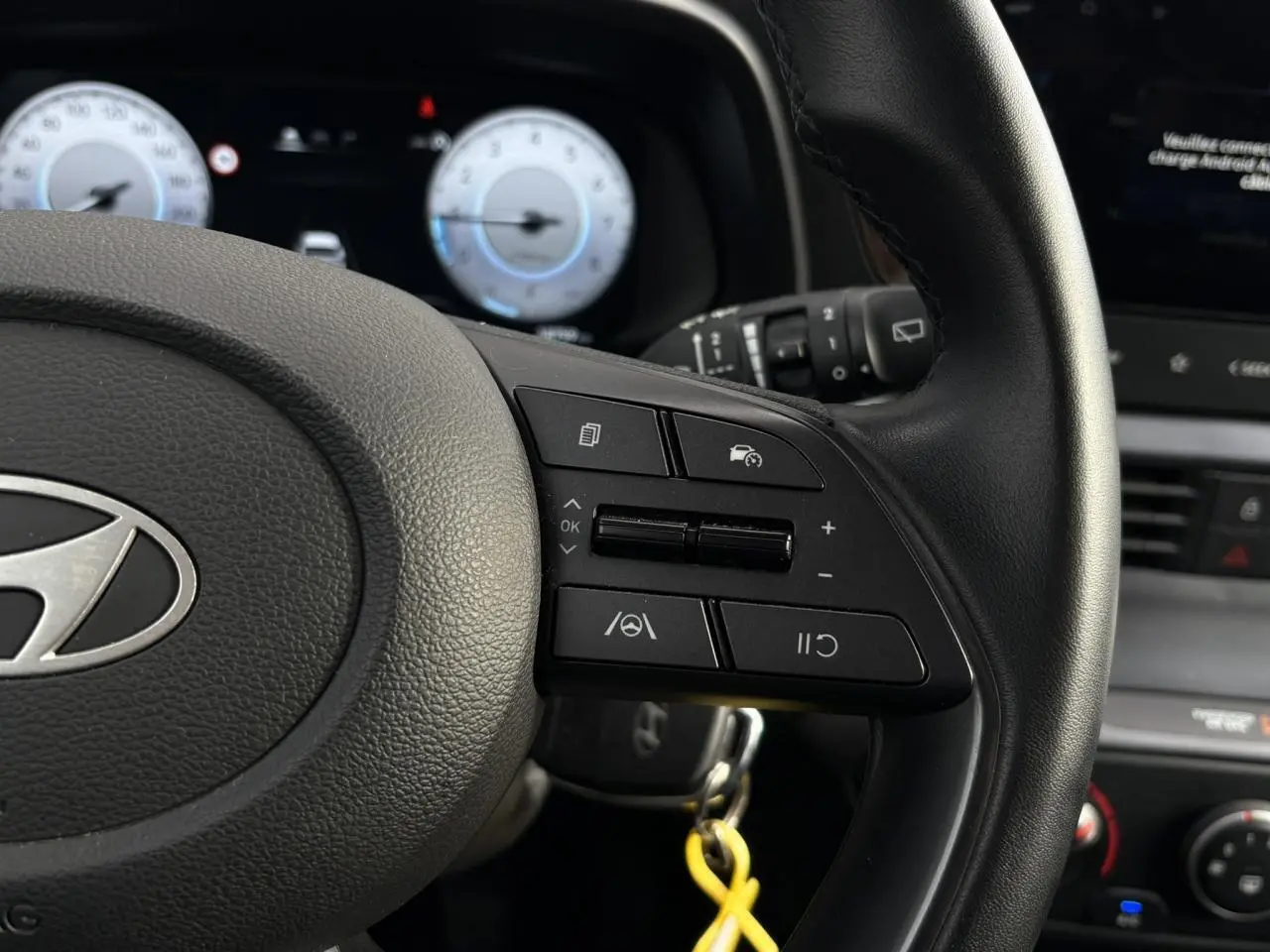 Gros plan sur le volant cuir de la Hyundai i20 2025, montrant les commandes au volant côté droit et le tableau de bord numérique.