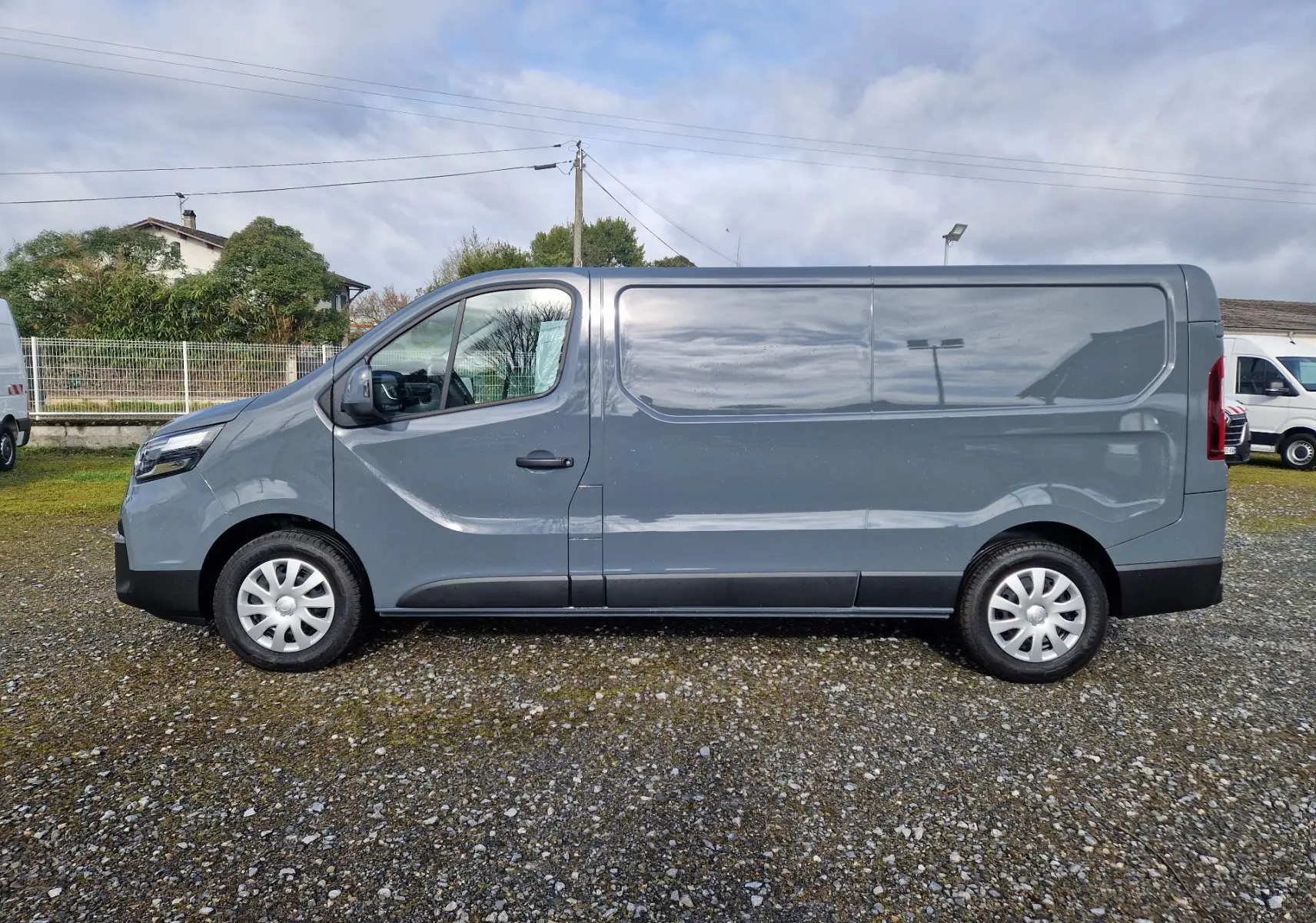 Vue latérale droite d’un utilitaire Nissan Primastar gris urbain 2025 avec porte coulissante et jantes acier.