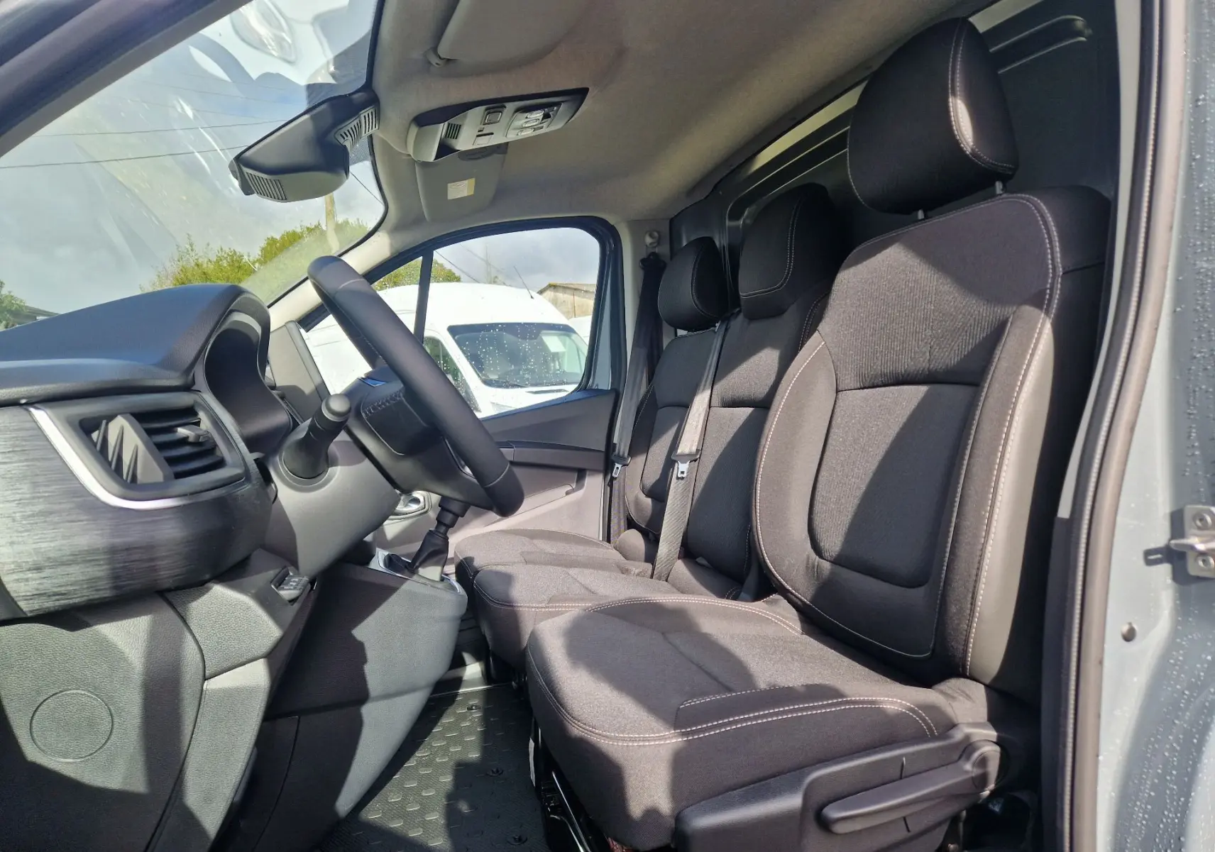 Vue intérieure côté conducteur du Nissan Primastar gris urbain 2025, montrant les sièges 3 places et le tableau de bord.