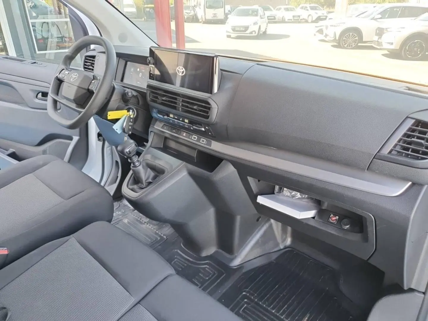 Vue intérieure côté conducteur du Toyota Proace Fourgon blanc Glacier, montrant le tableau de bord et la banquette avant grise.