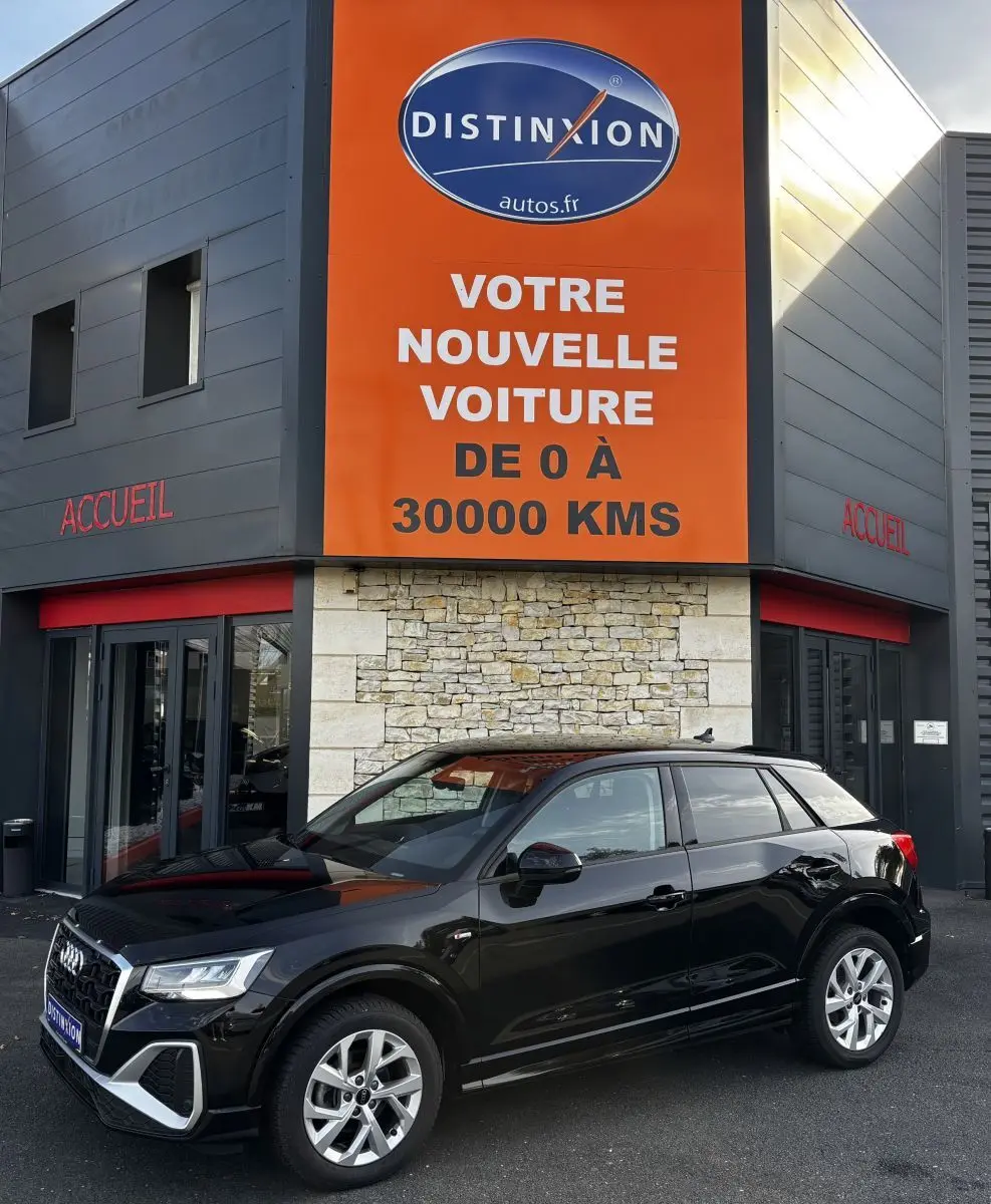 Audi Q2 noir vue 3/4 avant droit, garée devant un bâtiment avec panneau orange Distinxion.