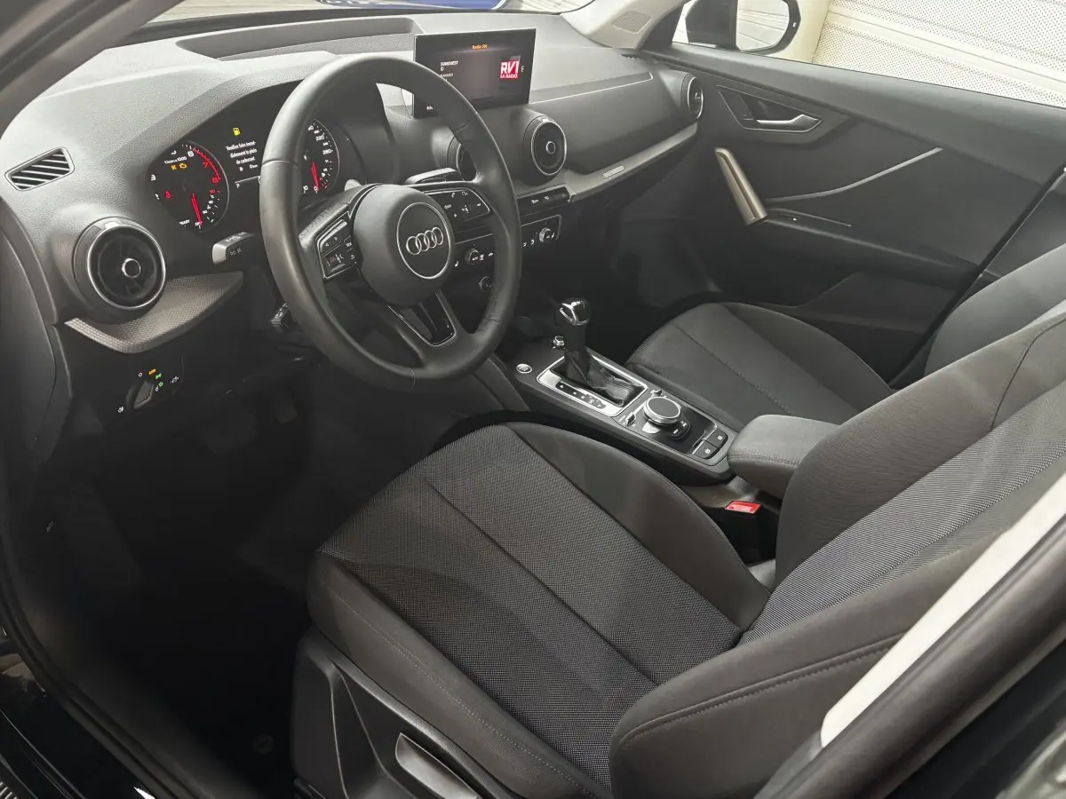 Vue intérieure côté conducteur de l'Audi Q2 noir 35 TFSI S Line 2023, avec tableau de bord digital et volant cuir multifonctions.