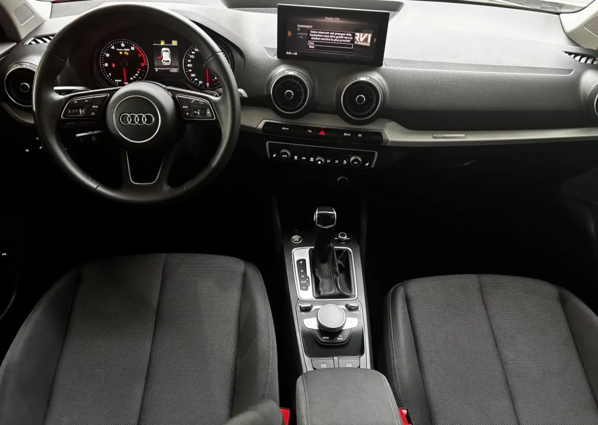 Vue intérieure de l'Audi Q2 35 TFSI S Line 2023, tableau de bord noir avec volant cuir et console centrale moderne.