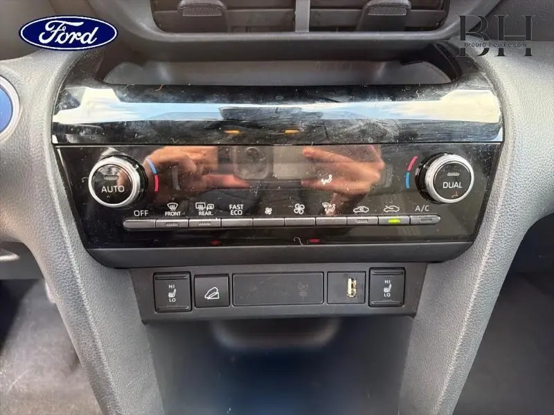 Panneau de commande de climatisation bi-zone avec boutons et réglages, intérieur noir brillant, vue frontale rapprochée.