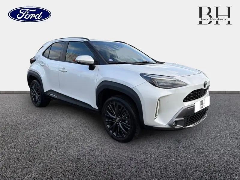 Vue 3/4 avant d'une Toyota Yaris Cross blanche nacrée avec jantes noires et protections noires sur les passages de roues.