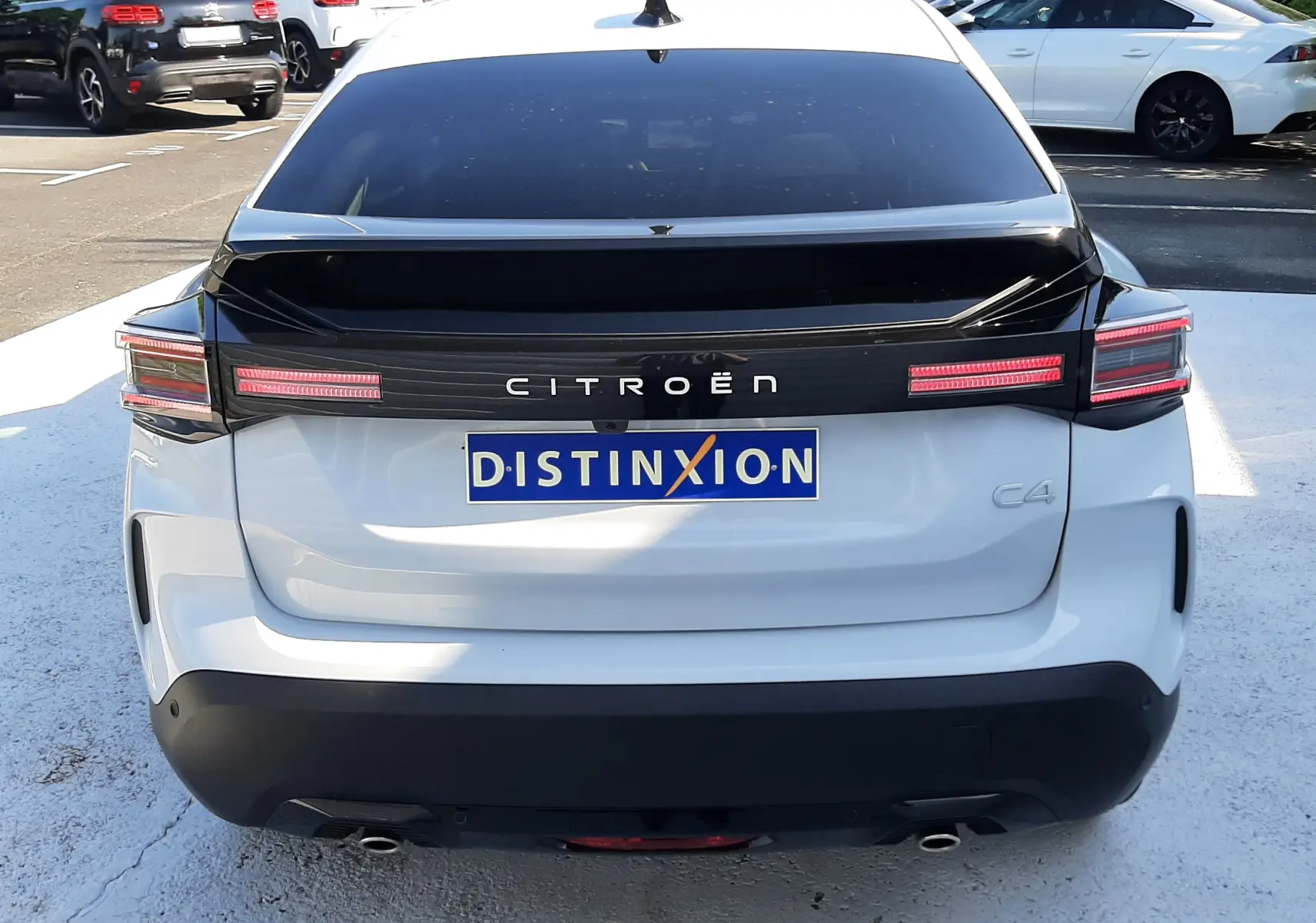 Vue arrière d'une Citroën C4 blanche Okenite avec bande noire et feux LED caractéristiques, stationnée en extérieur.