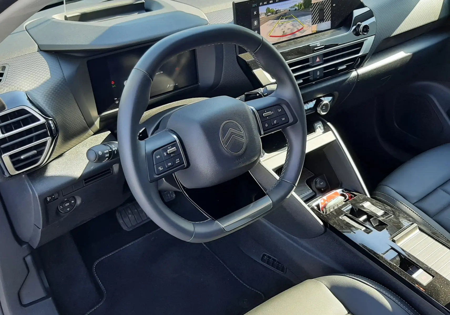 Vue intérieure côté conducteur du tableau de bord et volant noir de la Citroën C4 hybride 2025 avec écran tactile et sellerie cuir.