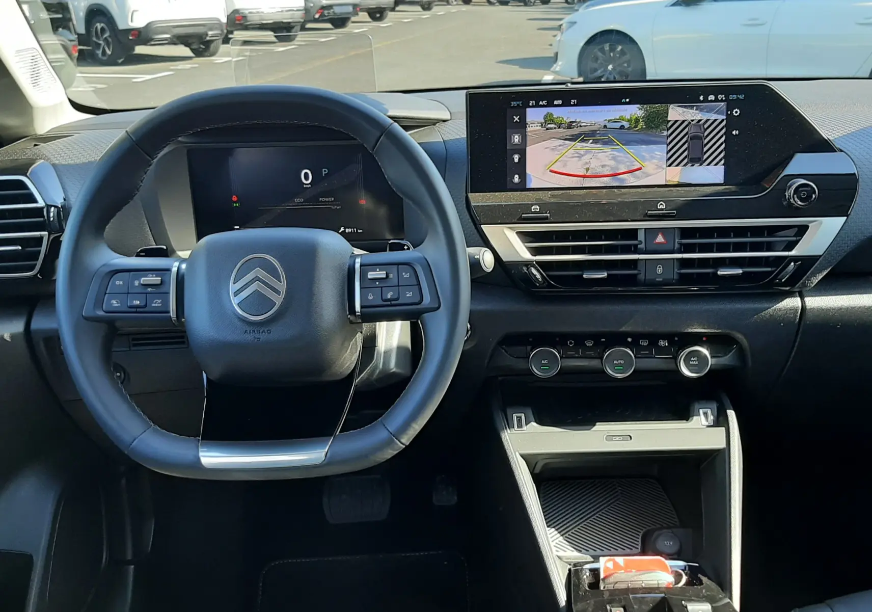 Vue intérieure du poste de conduite du Citroën C4 blanc Okenite 2025, avec tableau de bord numérique et écran central affichant la caméra de recul.