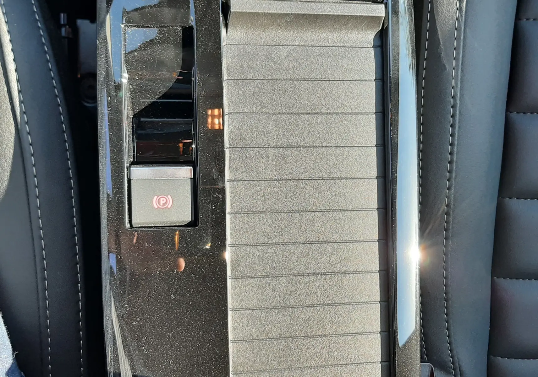 Gros plan sur la console centrale noire brillante de la Citroën C4 hybride, avec bouton frein à main électrique et accoudoir gris.