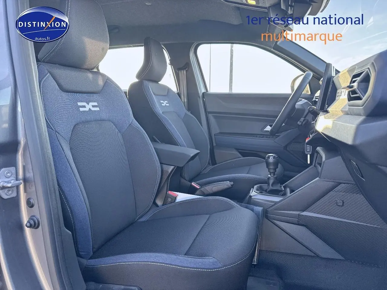 Vue intérieure côté conducteur du Dacia Duster 2025 avec sièges tissu gris et accoudoir central avant.