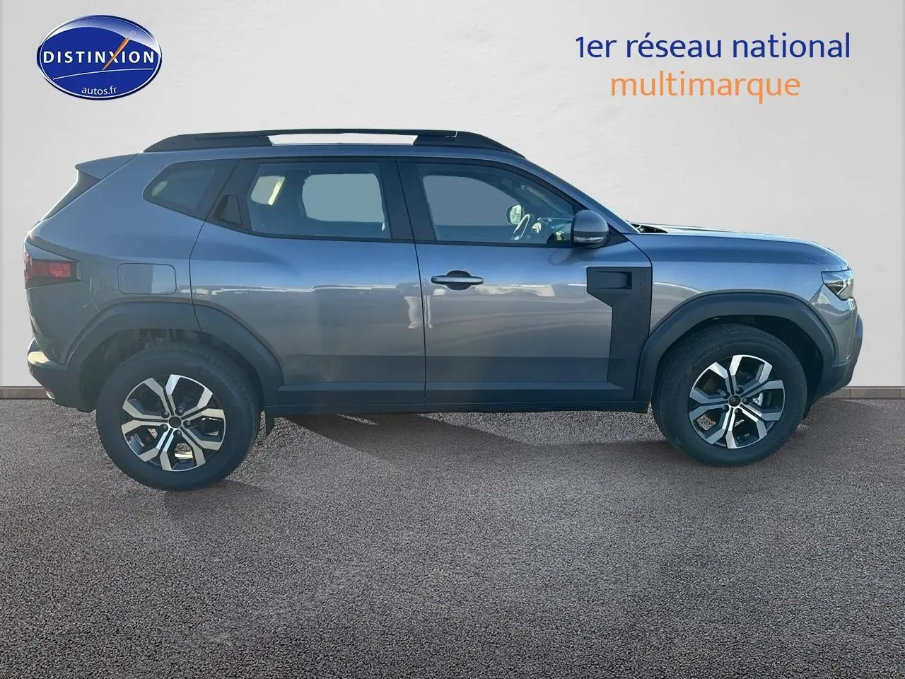 Profil droit du Dacia Duster gris schiste 2025 avec jantes alu et barres de toit visibles.
