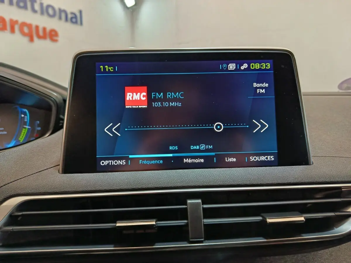 Écran tactile central affichant la radio FM RMC dans l’habitacle du Peugeot 3008 bleu, vue de face.