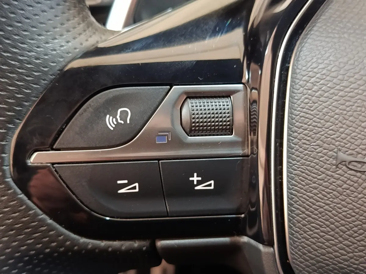 Gros plan sur les commandes vocales et volume au volant cuir noir du Peugeot 3008 bleu hybride rechargeable.
