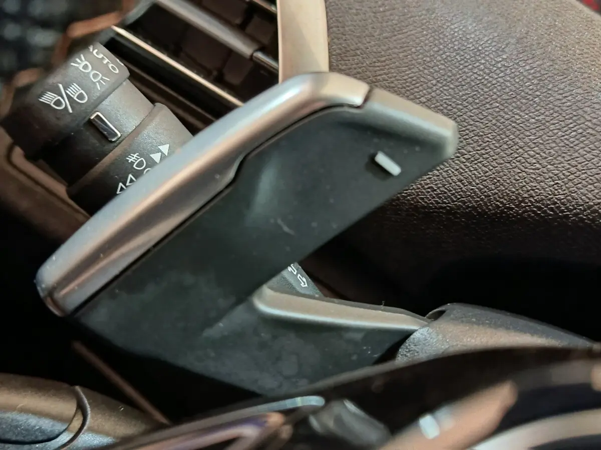 Gros plan sur la palette de changement de vitesse grise et les commandes des phares du Peugeot 3008 hybride bleu.