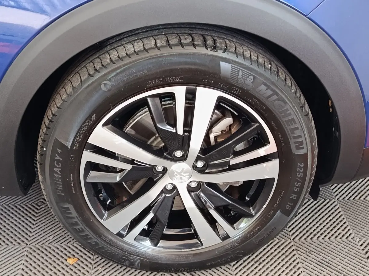 Gros plan sur la roue avant gauche du Peugeot 3008 bleu, avec jante alliage bicolore et pneu Michelin.